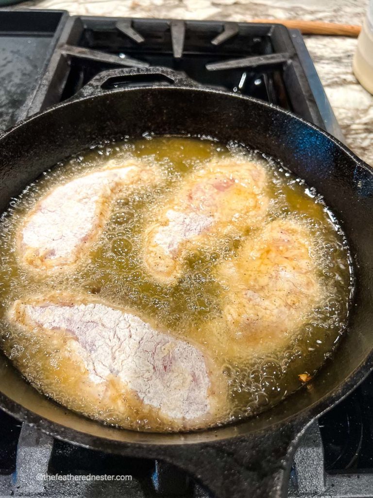 frying chicken in the oil on a cast iron skillet