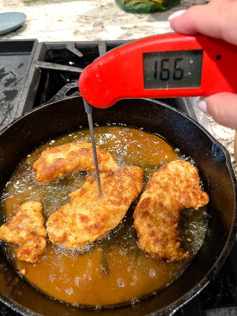 frying the chicken strips in a cast iron skillet with a instant read thermometer showing the  temperature of 166 degree Fahrenheit