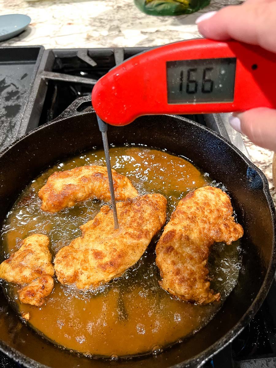 Frying the chicken strips in a cast iron skillet with a instant read thermometer showing the  temperature of 166 degree Fahrenheit.