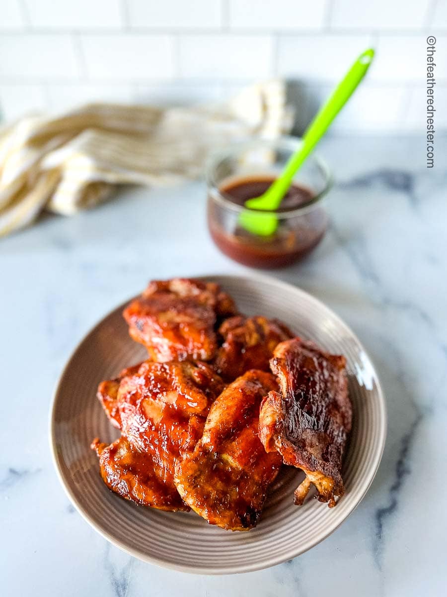 Chicken on a plate with 3 Ingredient Homemade BBQ sauce on a medium bowl with a basting brush.