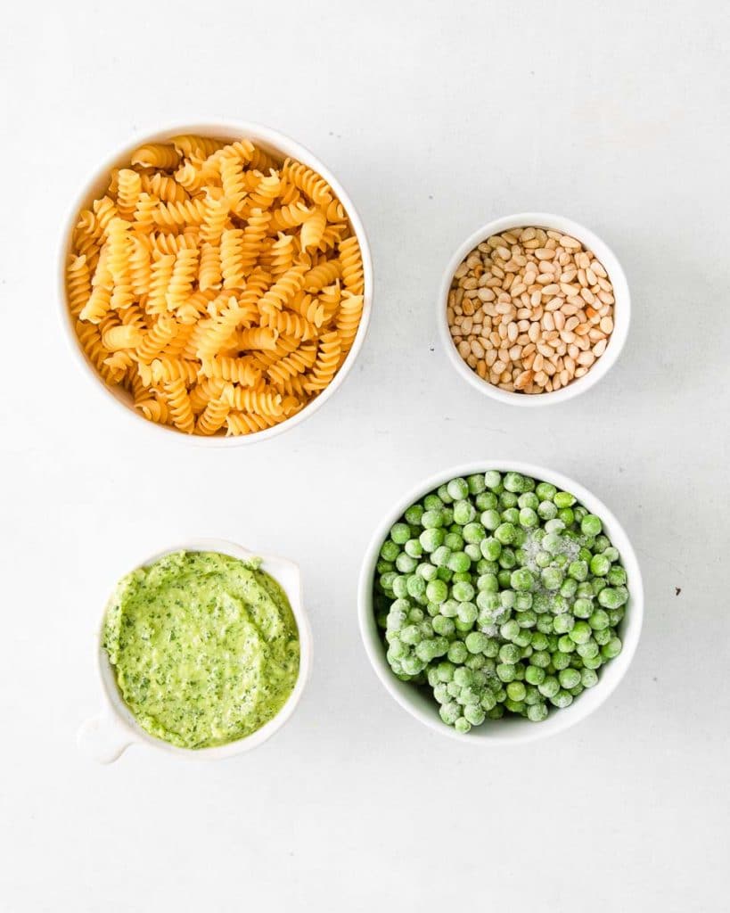 ingredients for cooking the summer pesto pasta salad which contains rotini pasta, green peas, toasted pine nuts, and pesto sauce.