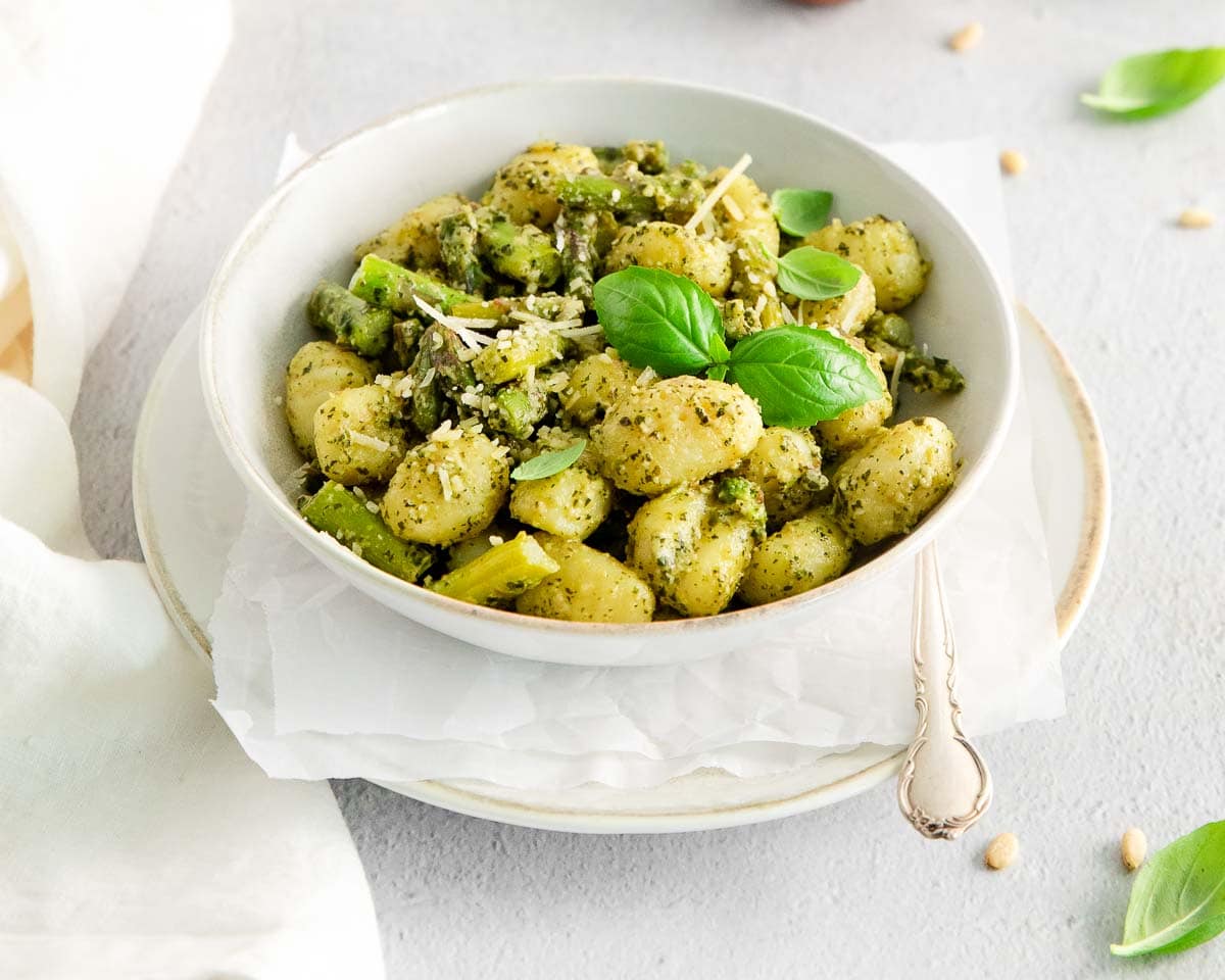 a white bowl of potato pasta with asparagus.