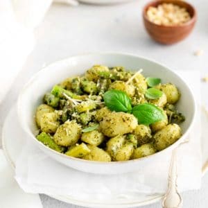 a white bowl of pesto gnocchi with asparagus with a small bowl of parmesan cheese in the background
