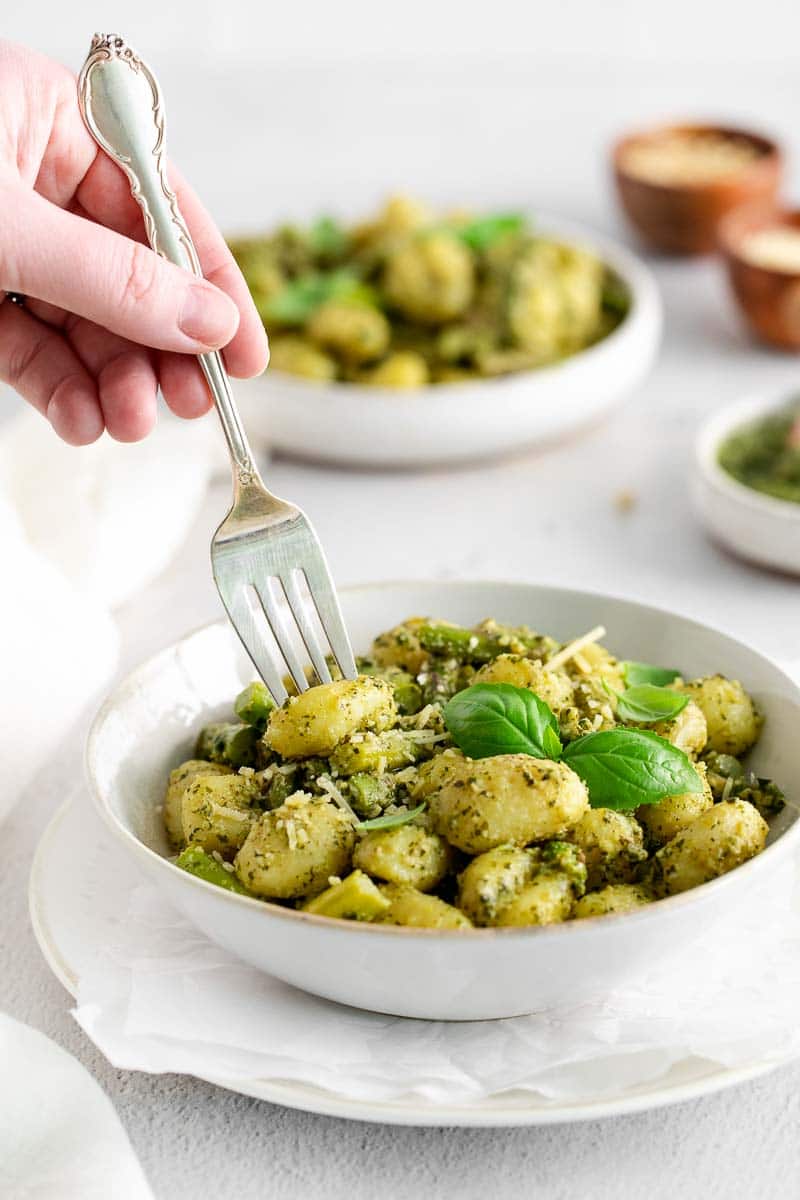 Woman's hand holding a fork in a bowl of pesto gnocchi.