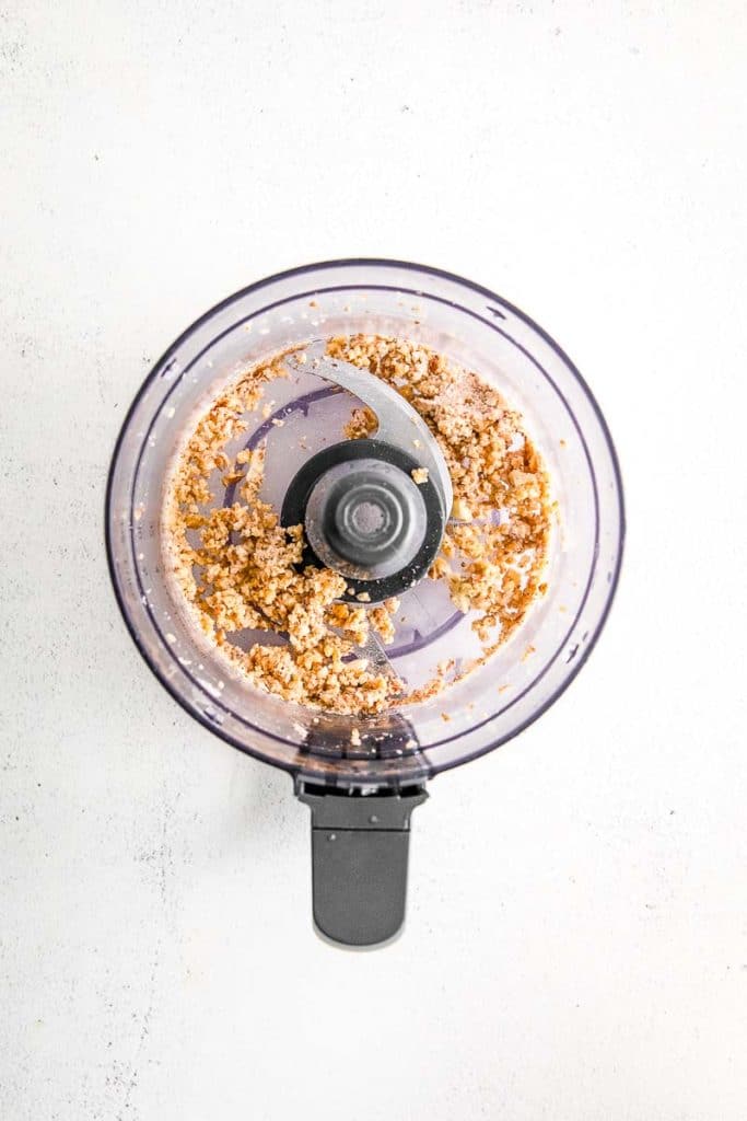 a food processor with crushed mixed pine nuts, garlic, and lemon juice inside.