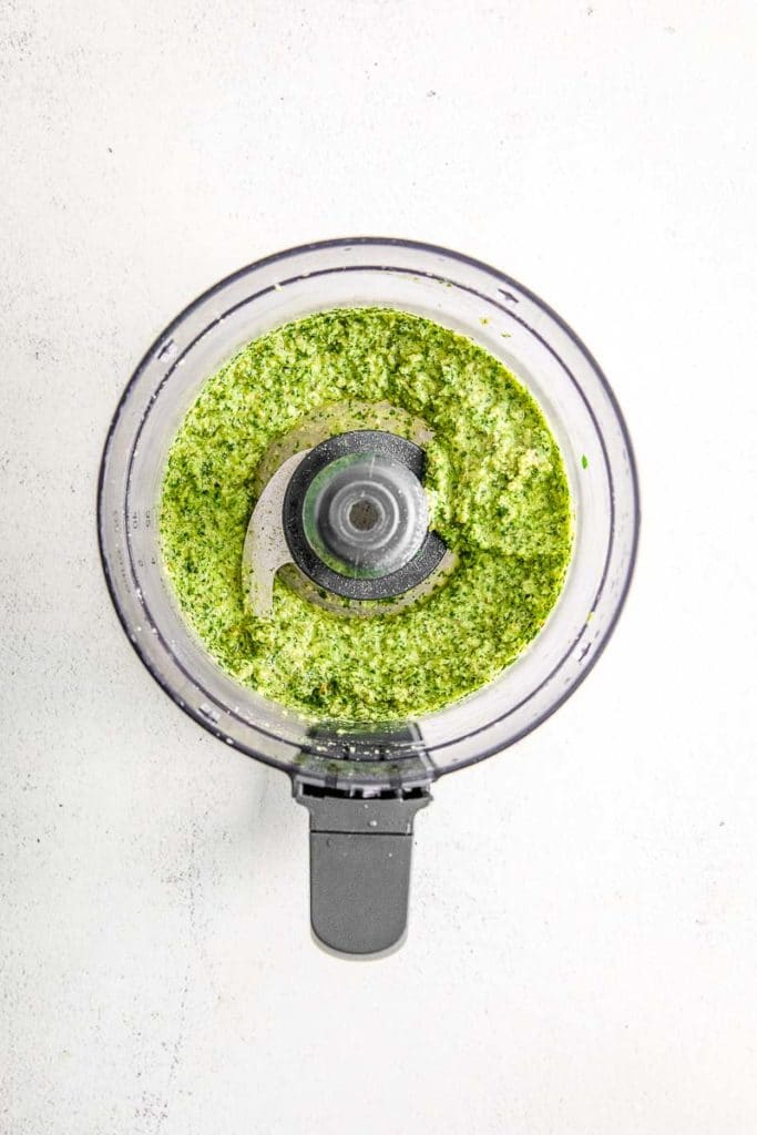 all mixed up ingredients for pesto sauce with olive oil in a food processor
