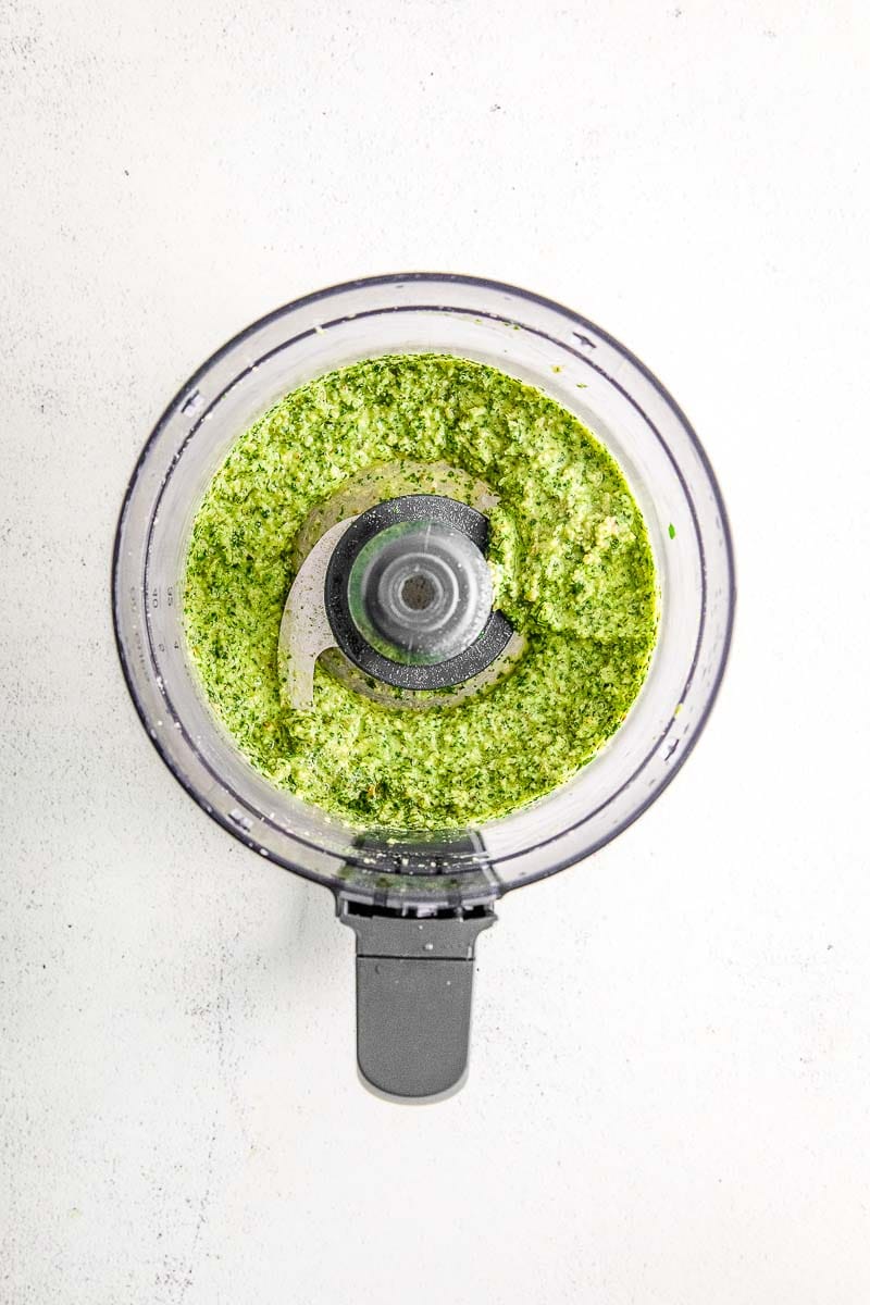 All mixed up ingredients for pesto sauce with olive oil in a food processor.