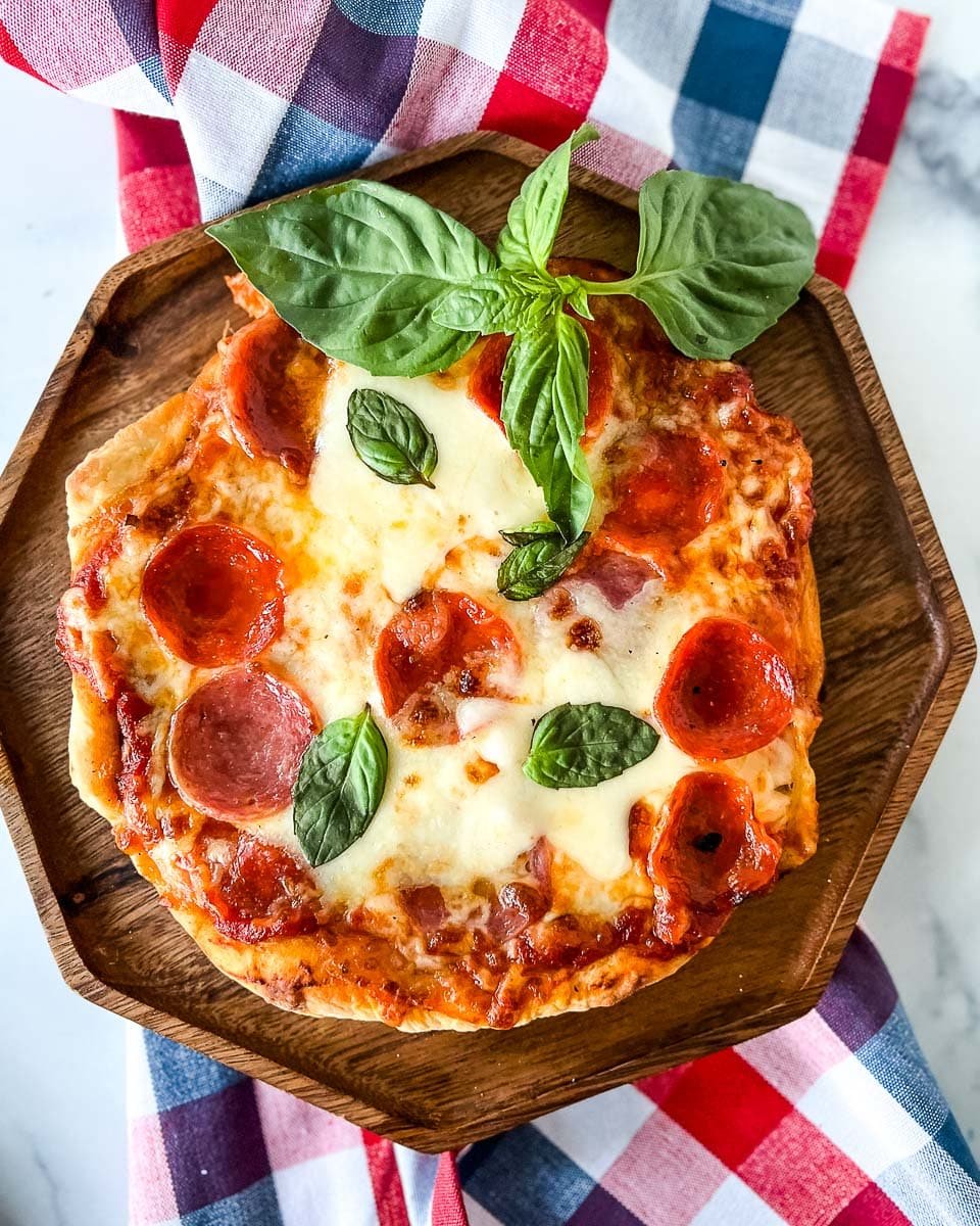 grilled pizza on a wooden serving tray with a sprig of basil and a red, white, and blue napkin in the background.
