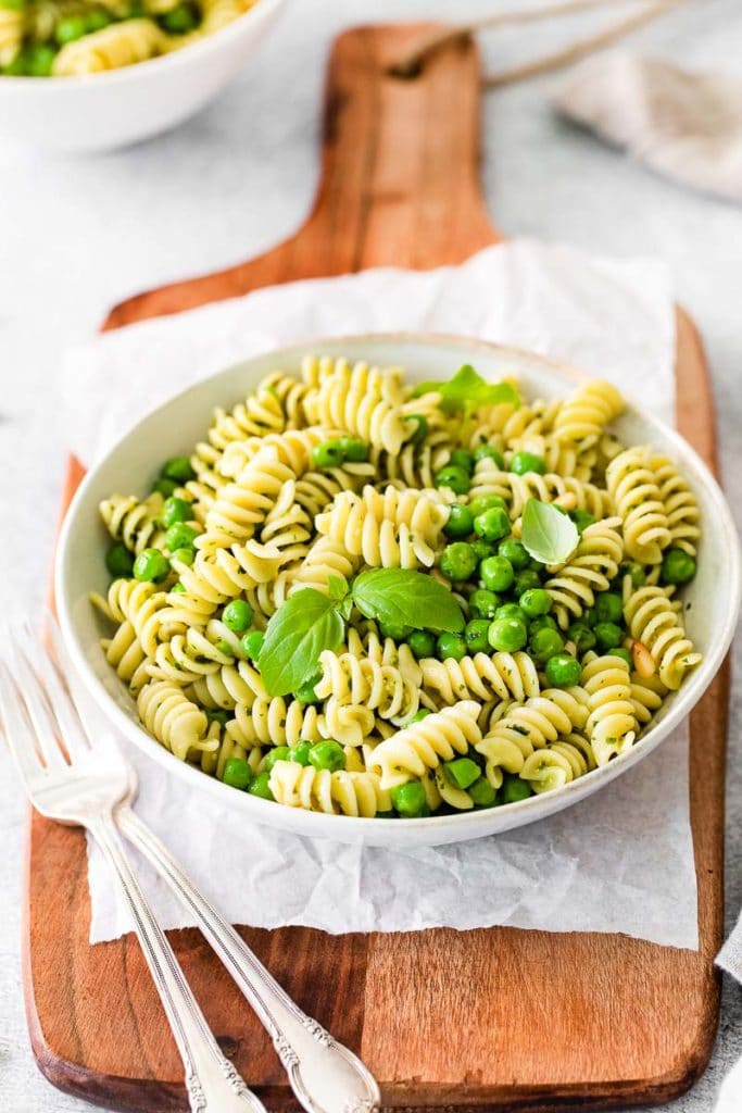 pesto rotini and silverwares on a white bowl on top of a wooden board