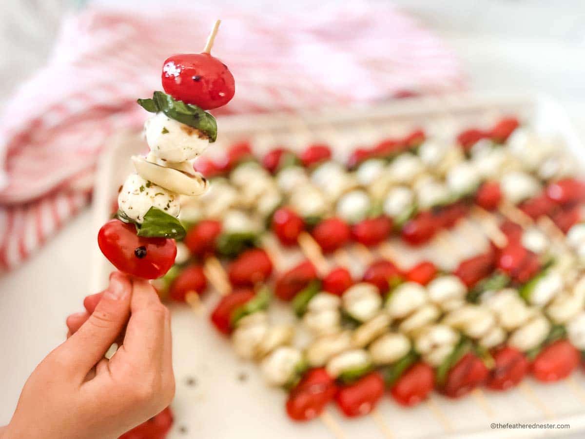 a closeup of a caprese tortellini appetizer with a tray of caprese skewers with balsamic drizzle and a red and white napkin in the background