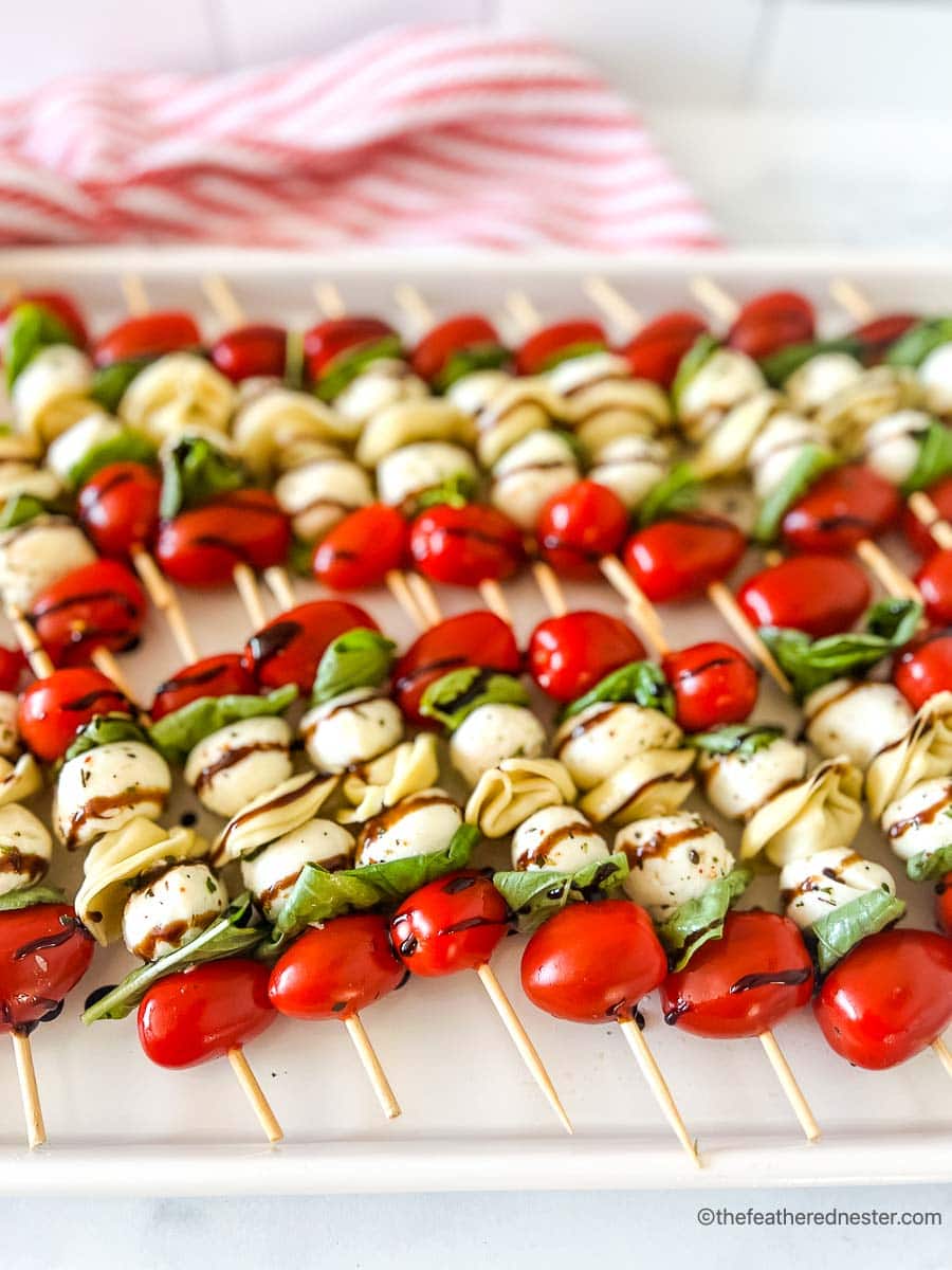 a white tray of tortellini skewers with balsamic glaze on top of a red and white napkin.