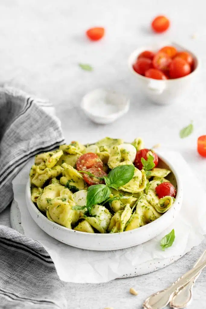 a white bowl of tortellini caprese salad with tomatoes and salt in the background.