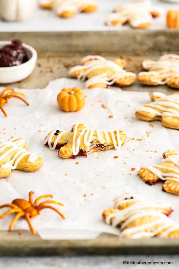 Halloween hand pies with berry fillings placed on a parchment paper and baking sheet with spider toy, pumpkin toy and a bowl of berry filling at the background