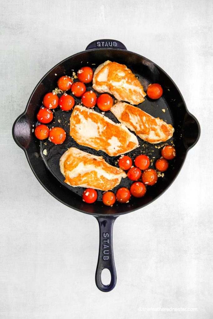 a Staub cast iron skillet with sautéed chicken breasts and cherry tomatoes