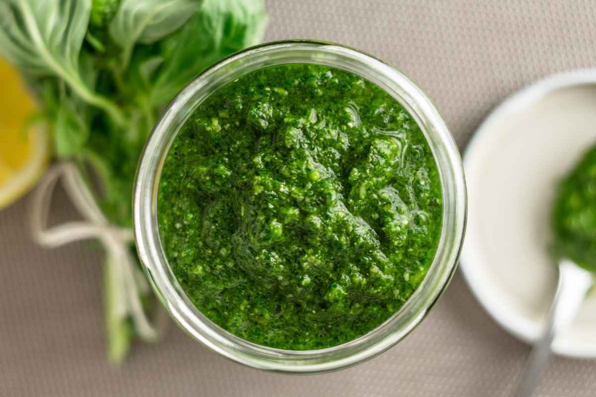 a jar of pesto sauce with a bunch of basil and a plate in the background.