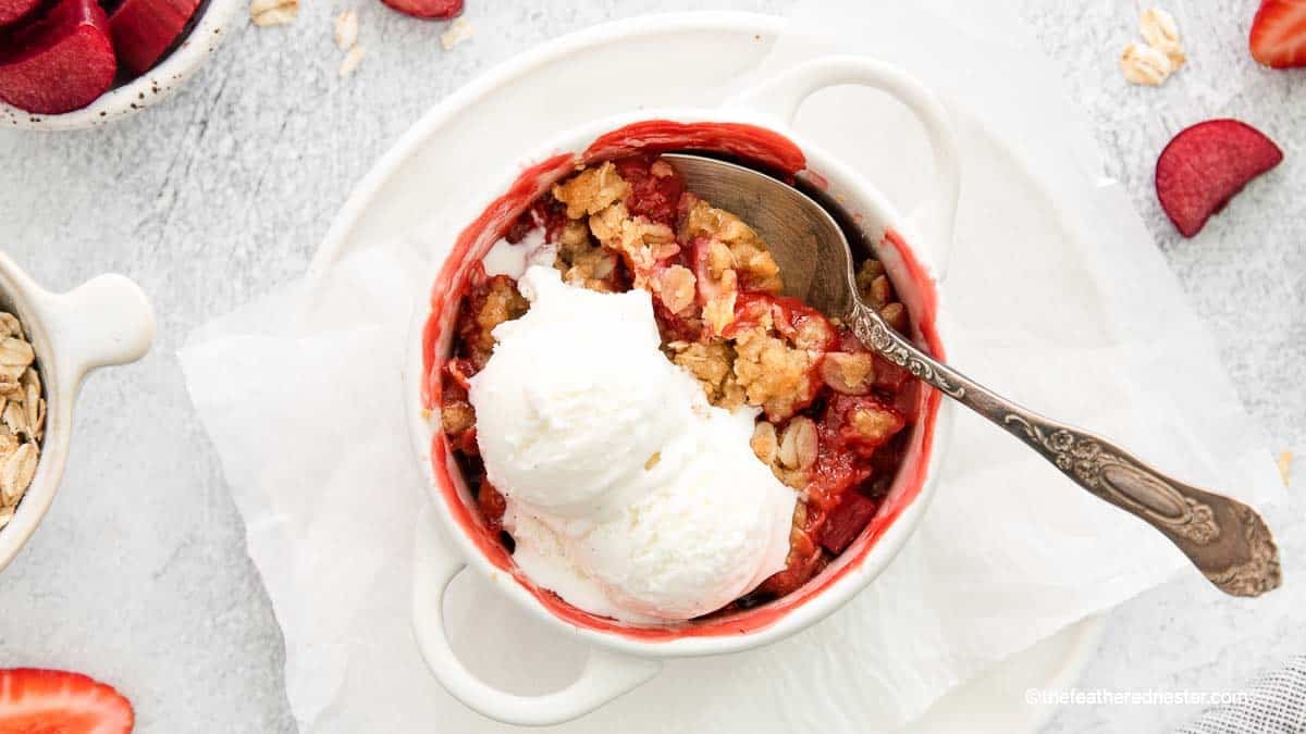 a white ramekin of apple strawberry cobbler with vanilla ice cream on top, and a spoon ready to serve it.