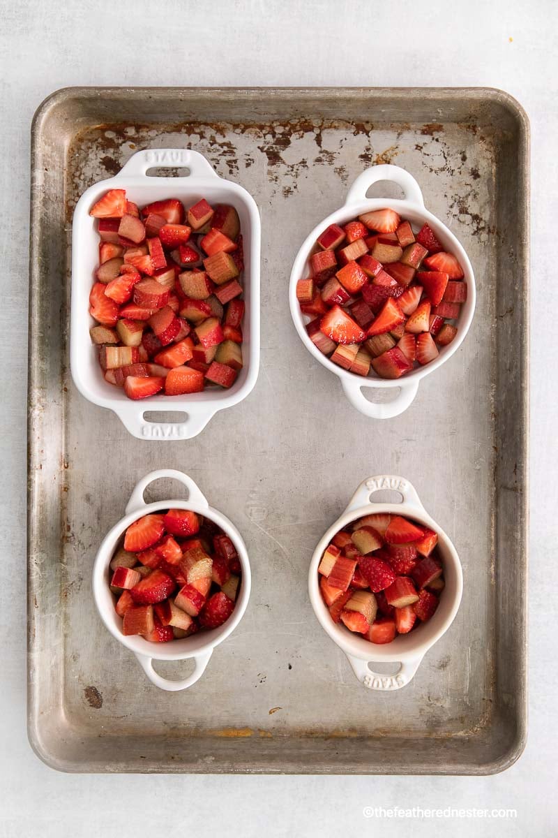 chopped strawberries and apple in ramekins and casserole on top of a baking tray.