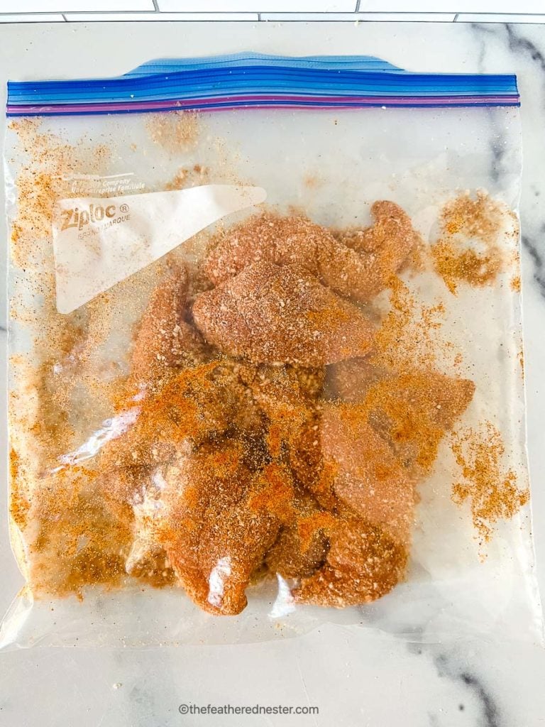 seasonings and chicken tenderloins mixed inside of a ziplock bag