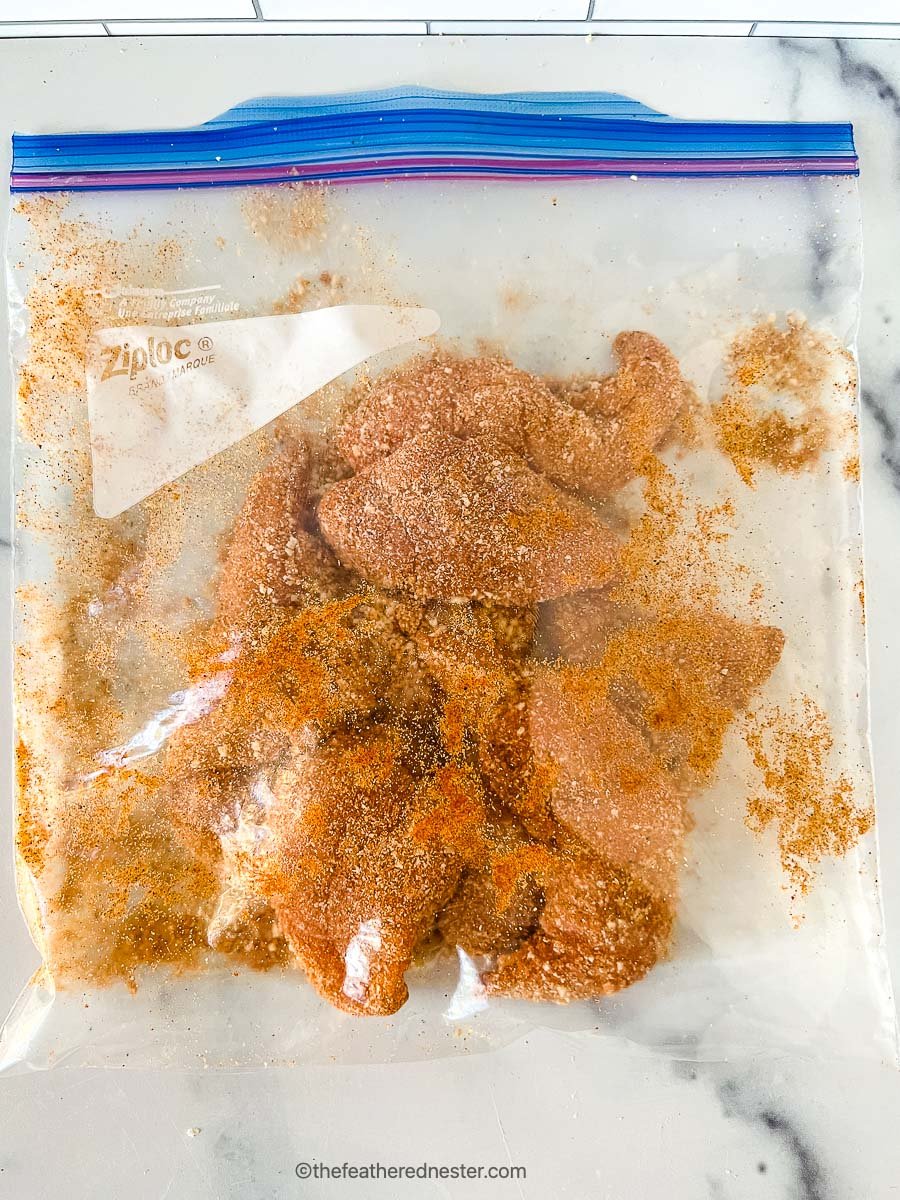 Seasonings and chicken tenderloins mixed inside of a ziploc bag.