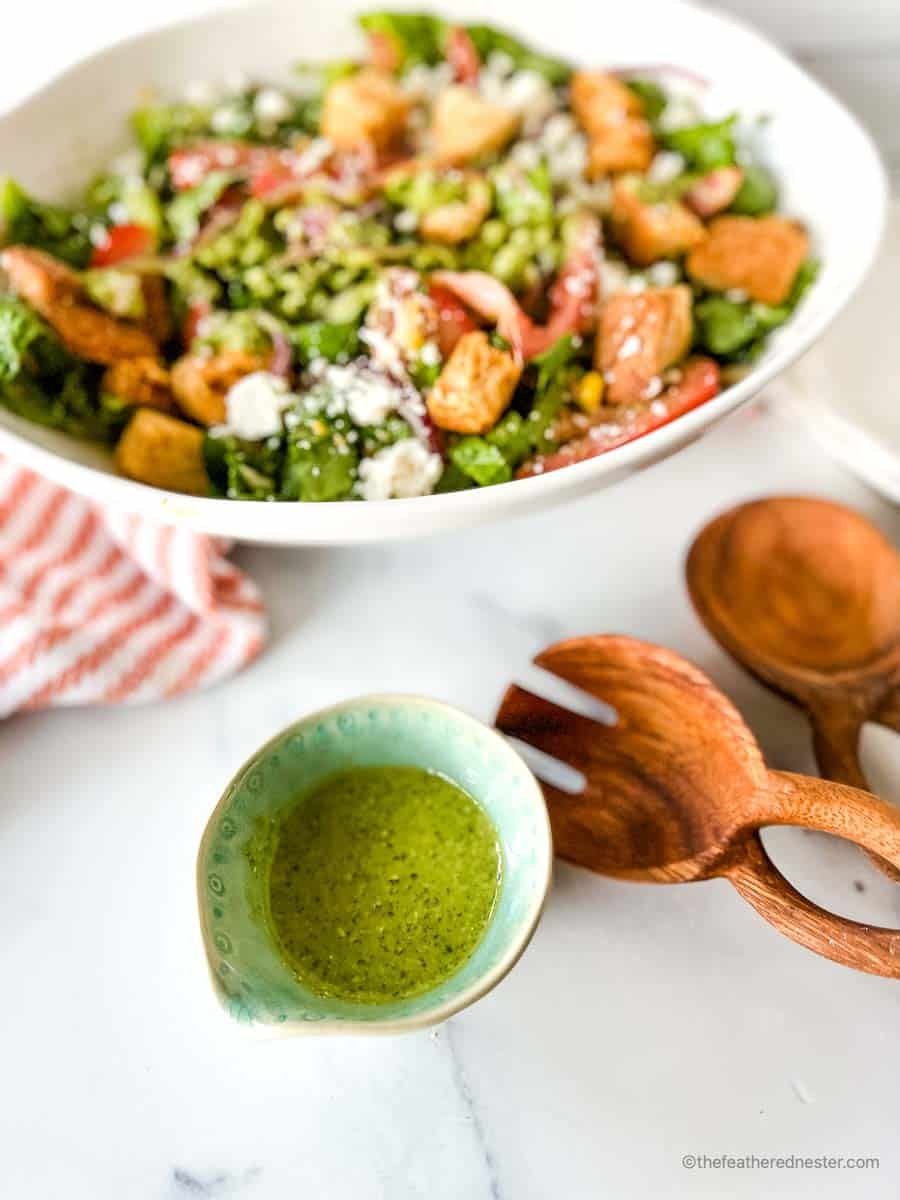 Pesto vinaigrette with Salad, wooden utensils, and a striped red cloth at the back.