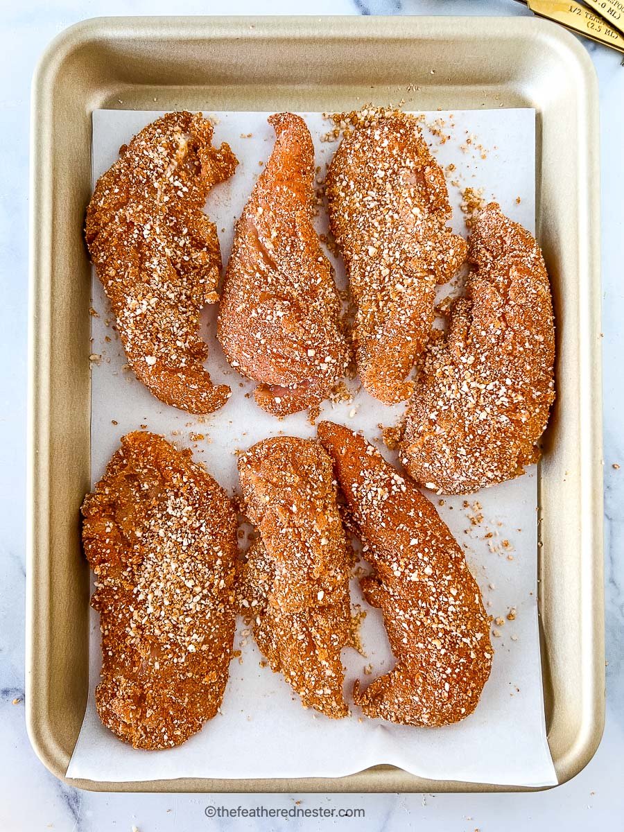 Large pieces of breaded poultry on baking sheet.