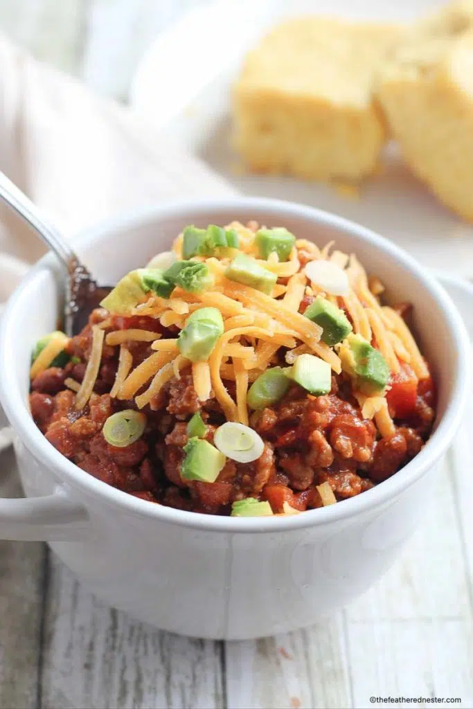 chili con carne and a silver spoon on a small bowl with cornbread in the background