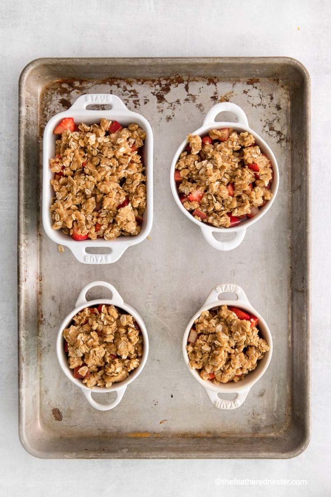 prepared fruit layer and oat crumble in ramekins and casserole on top of a baking tray