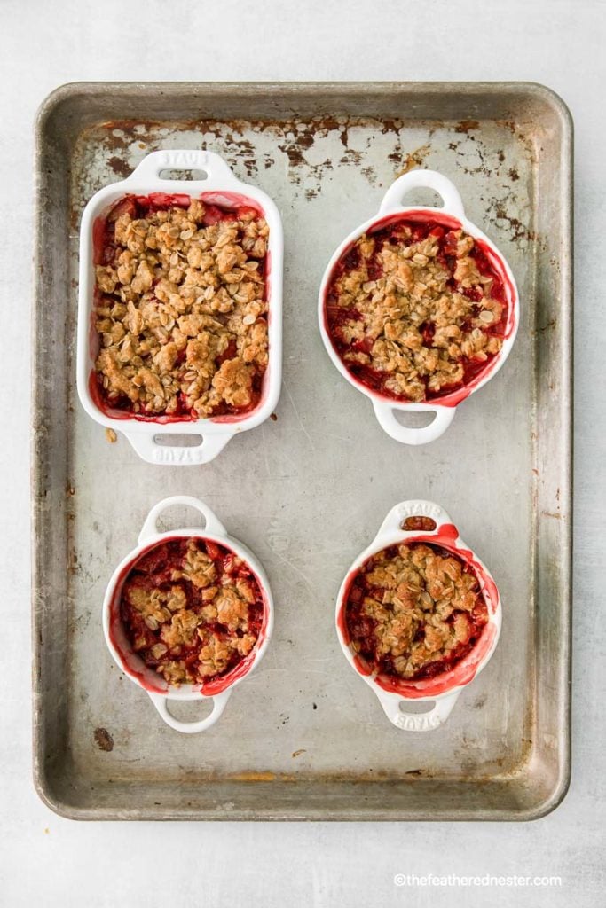 baked apple strawberry crisp in ramekins and casserole on top of a baking tray