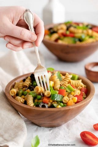 Zesty Italian Pasta Salad on a wood bowl with hand using a fork and another bowl of pasta salad on the background