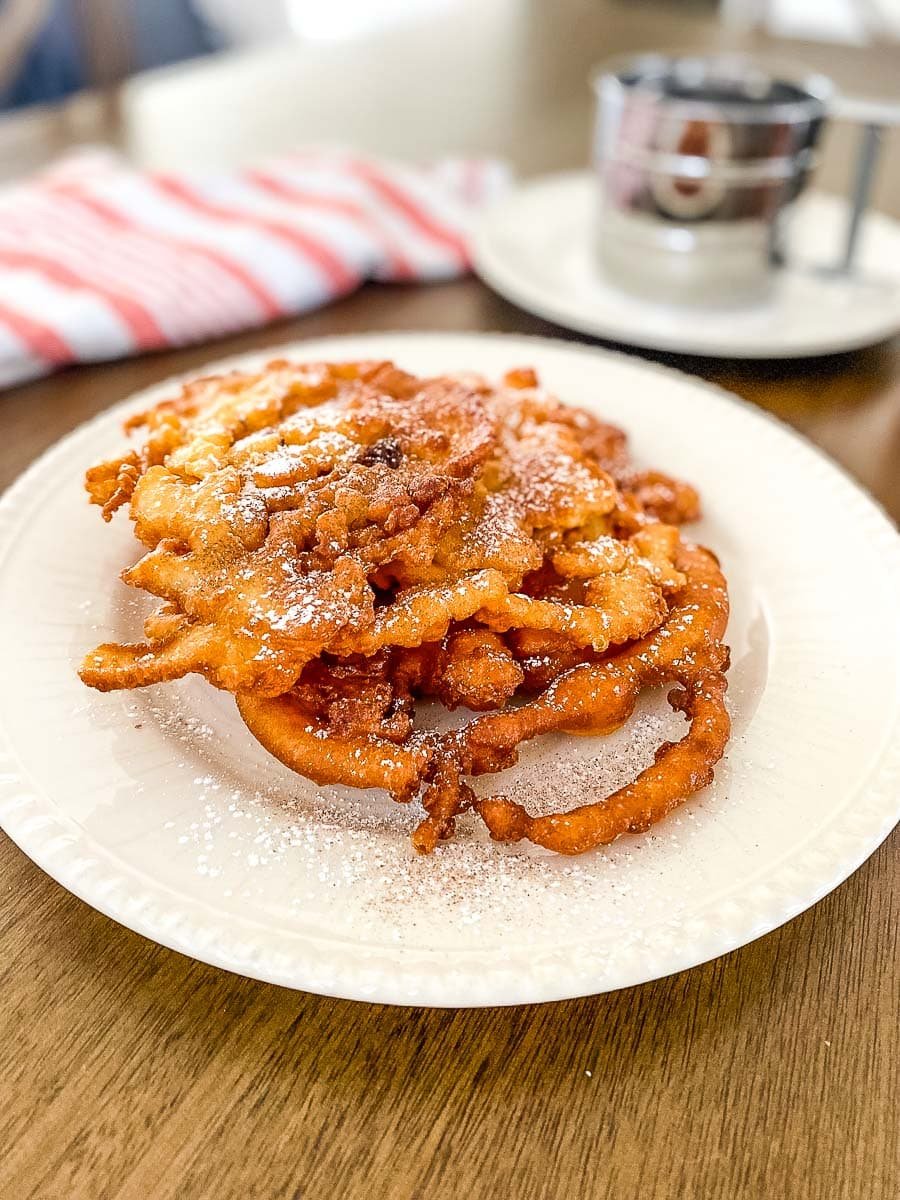 a white plate with homemade funnel cake and a striped red cloth and silver cup in the background.