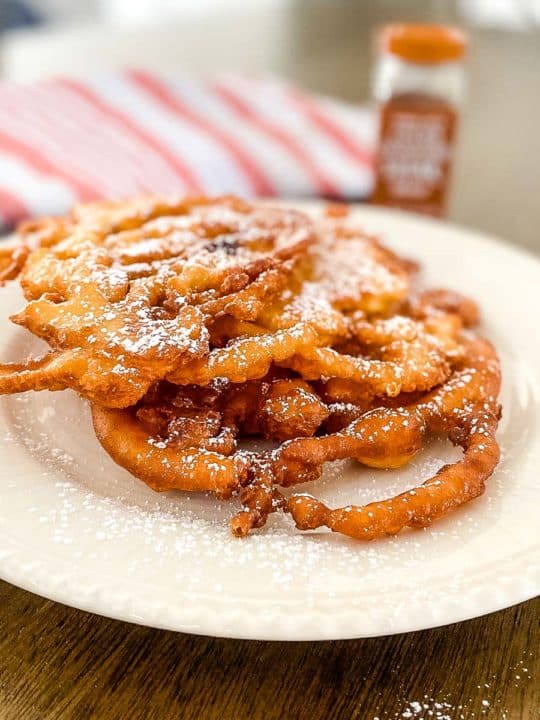 a white plate with Bisquick funnel cake and a red striped cloth and a cinnamon powder bottle at the back.