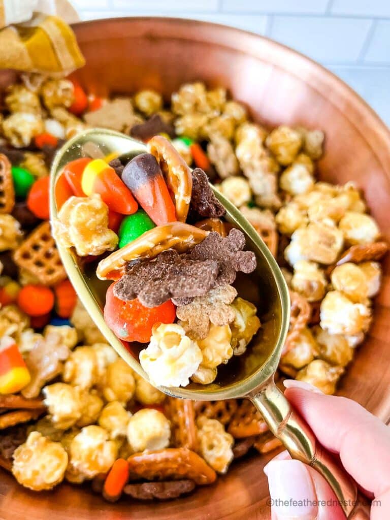 fall snack mix in a large copper bowl with someone scooping out some with a gold candy scoop
