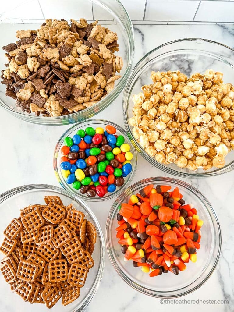 clear bowls of teddy grahams, crunch n munch, peanut M and Ms, candy corn with candy pumpkins, and pretzel grids