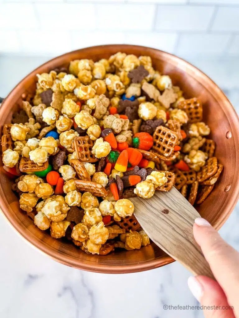 Stirring up the halloween snack mix ingredients in a copper bowl with a wooden spoon