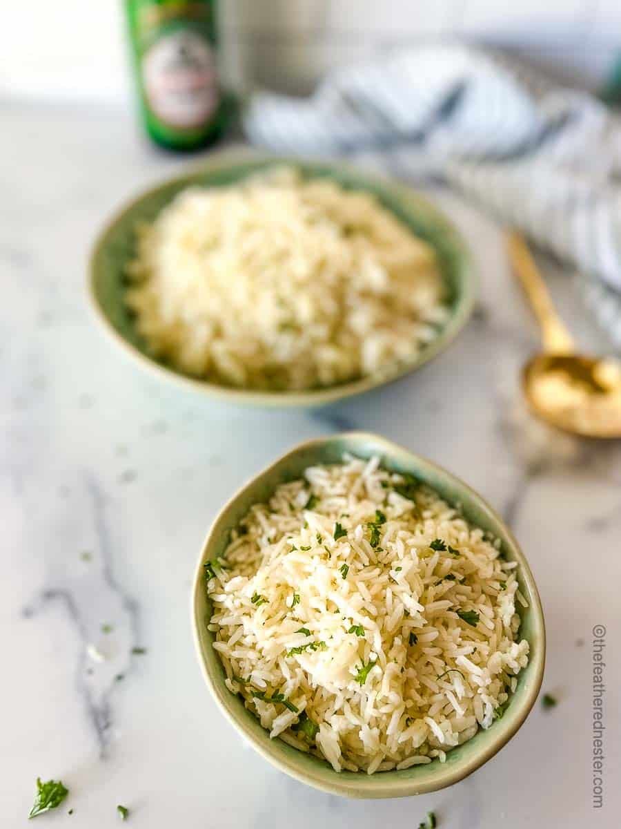 A green bowl with Instant Pot Jasmine rice and a golden serving spoon, striped cloth, bottle of soy sauce, and another large bowl of rice at the side.