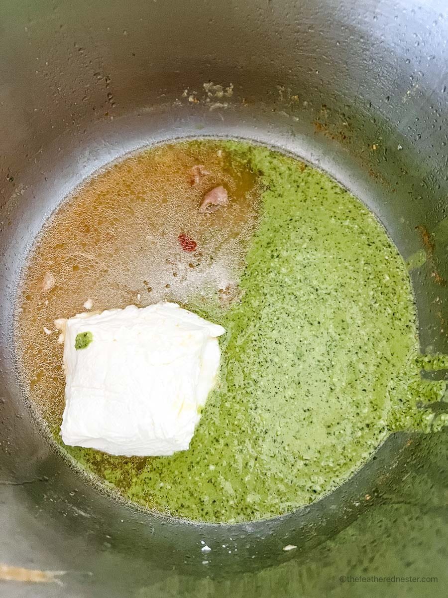 Chicken broth, cream cheese, and pesto sauce inside an Instant Pot.