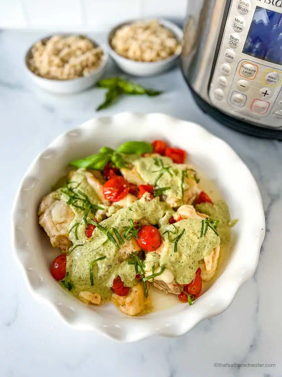 a white plate with Instant Pot Pesto Chicken with two bowls or rice and Instant Pot in the background.