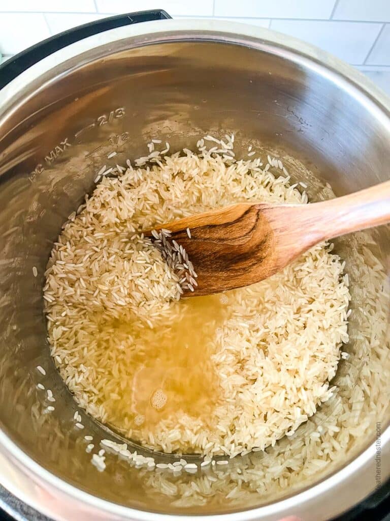 Using wooden spoon to stir broth into a pressure cooker of grains.