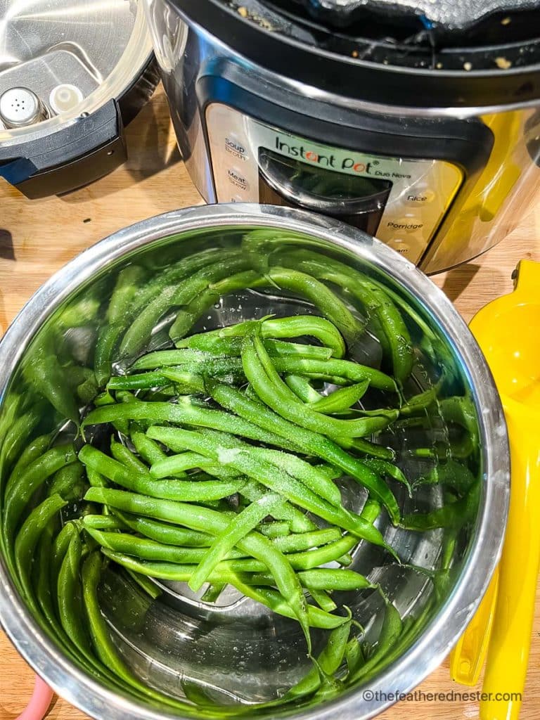 fresh green beans with salt on a steaming basket with instant pot in the background.