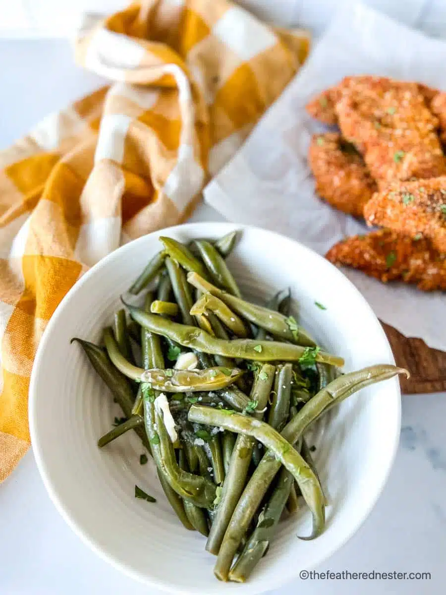 instant pot fresh green beans in a bowl with shake and bake chicken tenders and yellow cloth in the background.