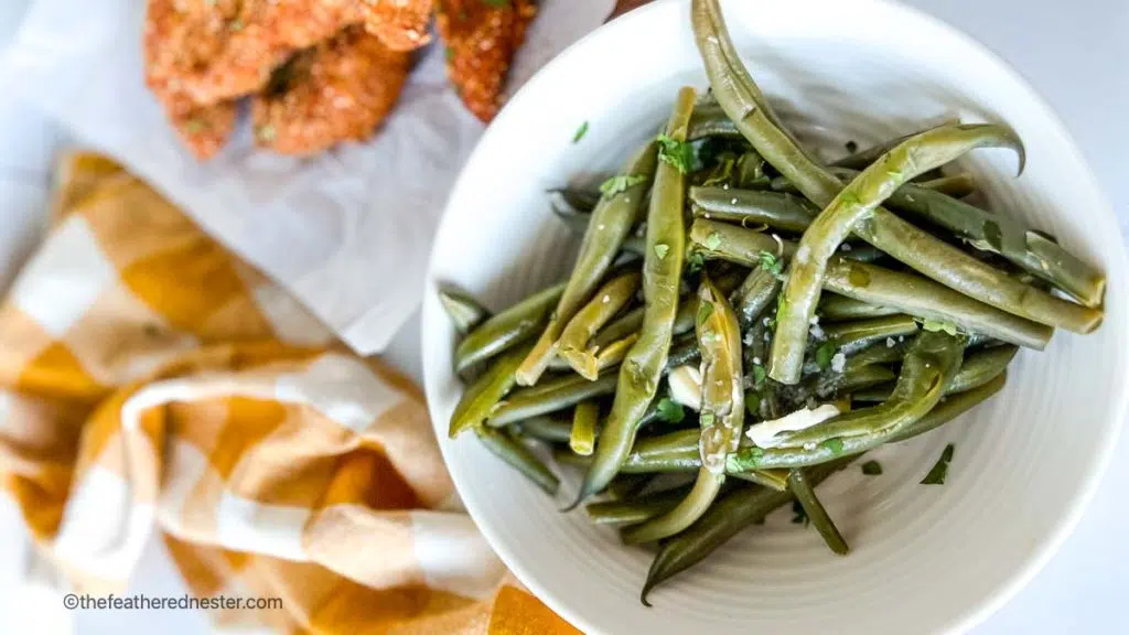 horizontal photo of instant pot fresh green beans in a bowl with shake and bake chicken tenders and yellow cloth in the background.