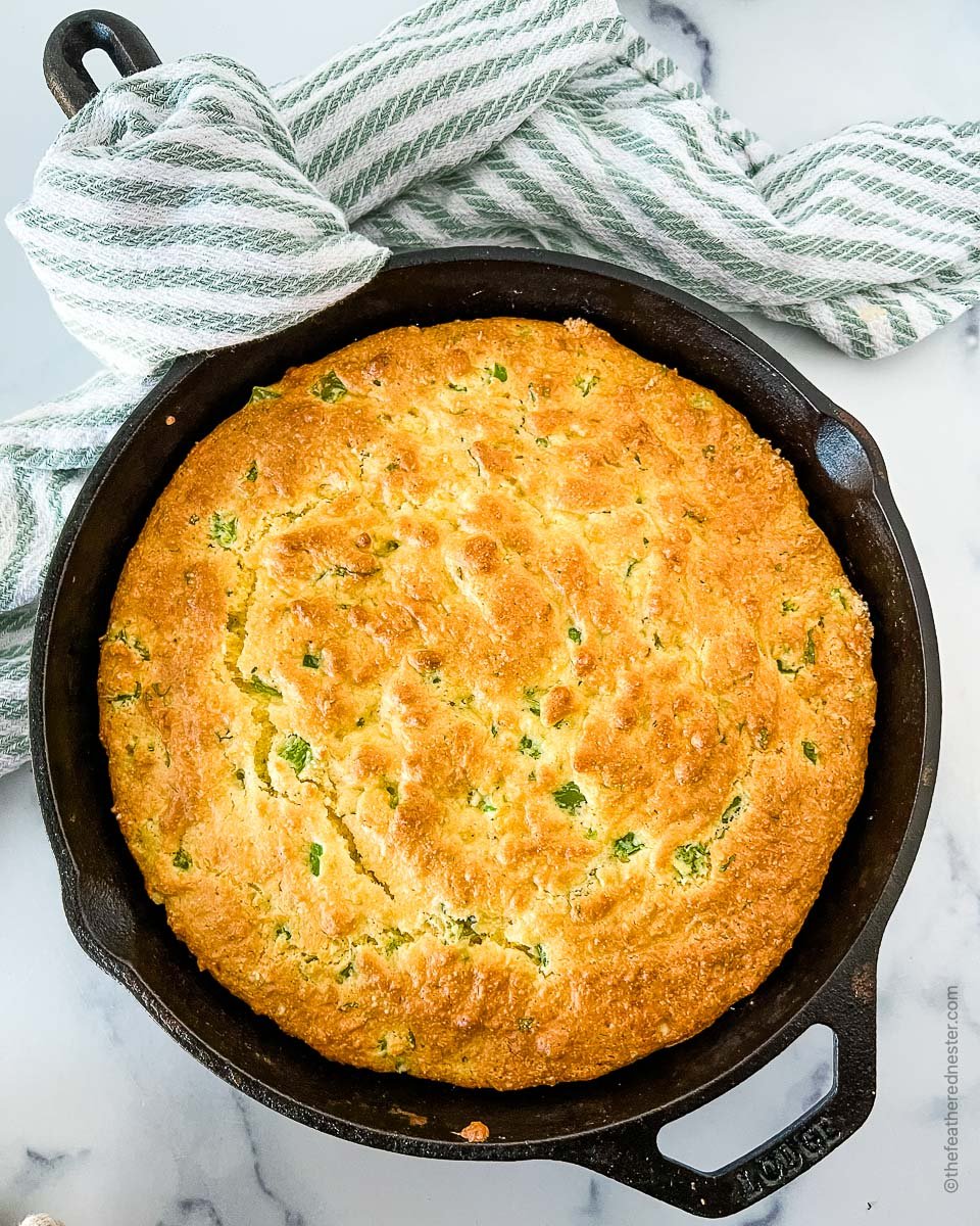 baked Jiffy jalapeno cheddar cornbread in a skillet with a striped cloth in the background.