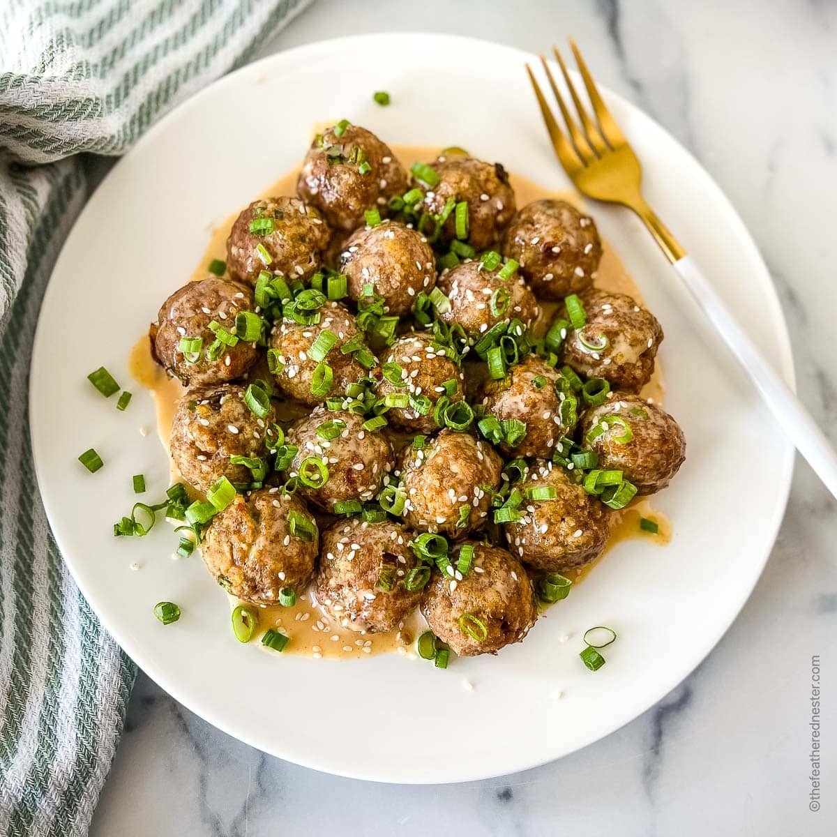 a white platter with chicken meatballs covered with creamy sriracha sauce and topped with green onions and sesame seeds.