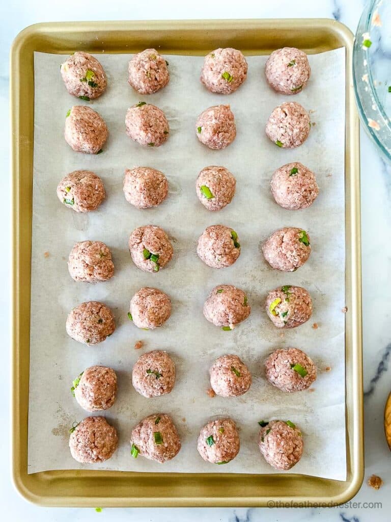 a baking sheet of 28 chicken balls ready to bake