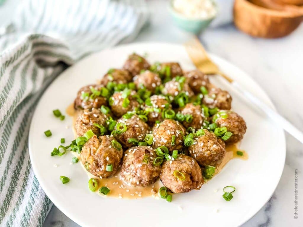 a white platter with spicy meatballs covered with creamy sriracha sauce and topped with green onions and sesame seeds
