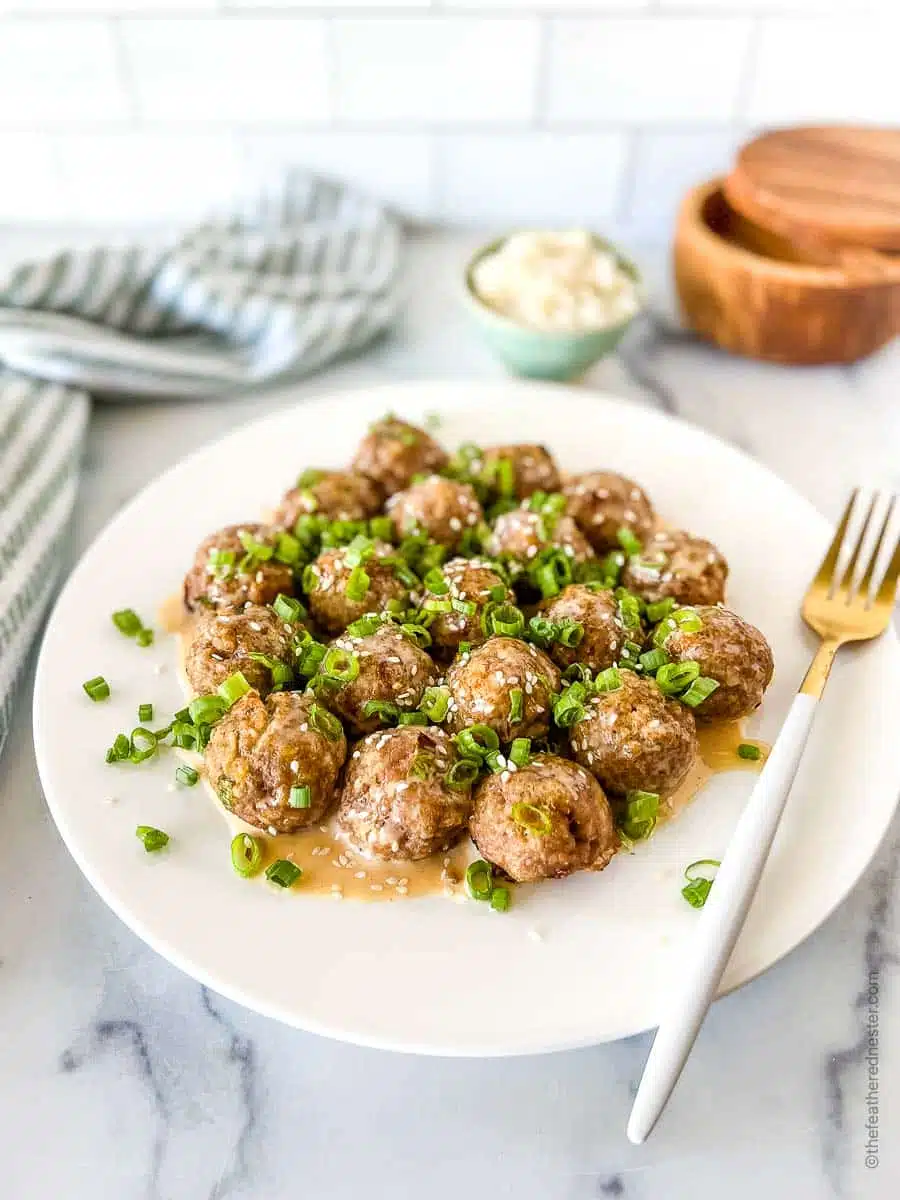 a white platter with spicy meatballs covered with creamy sriracha sauce and topped with green onions and sesame seeds