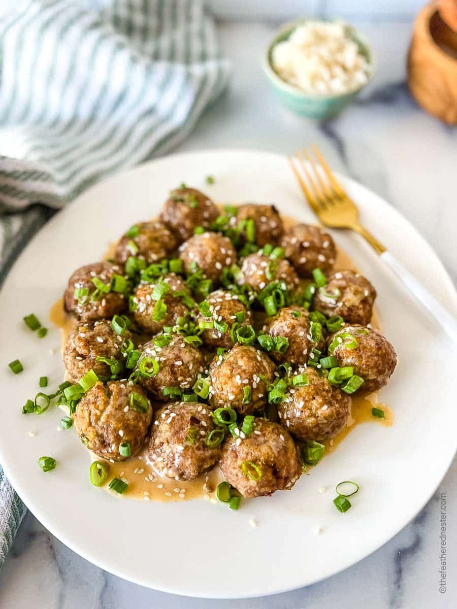 a white platter of honey sriracha meatballs garnished with sesame seeds and green onions.