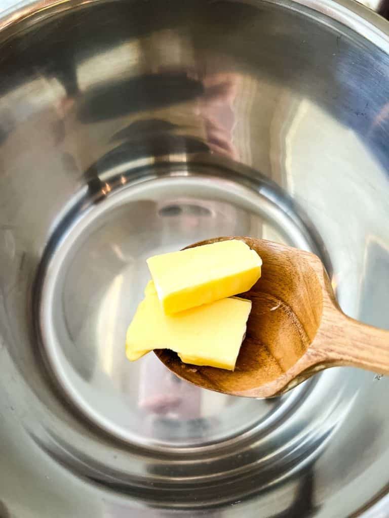 A wooden spoon putting a butter in the Instant Pot.