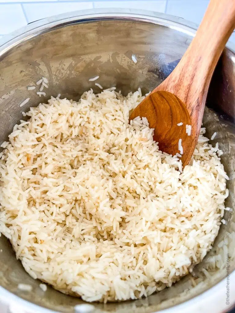 fluffing the cooked rice using a wooden spoon in the Instant Pot.