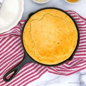 a cast iron skillet with cornbread with self rising flour and a striped red kitchen towel at the back.
